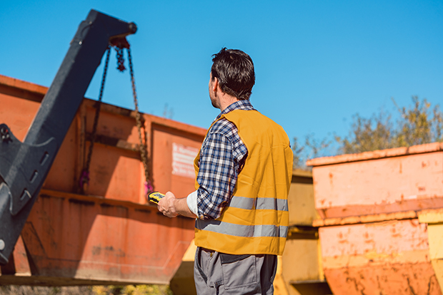 Worker on construction site unloading container for waste from truck using remote control